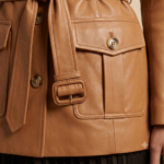 Close-up of tan leather safari jacket showing belt and flap pocket detail